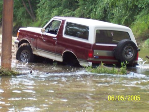 1990 Ford Bronco - A 1990 Ford Bronco navigates through a shallow body of water, with its spare tire mounted on the rear.