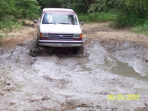 1990 Ford Bronco - A Ford Econoline van navigates a muddy trail on a wooded path.