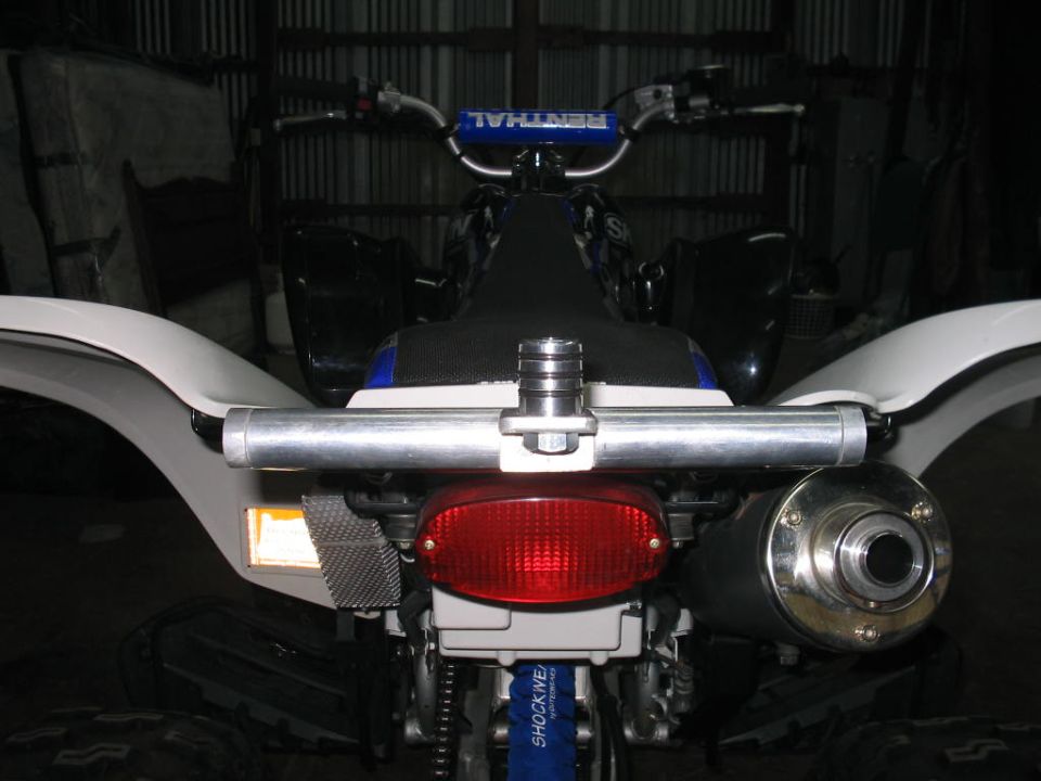 Rear view of a quad bike with a red taillight, silver exhaust, and white fenders. Handlebars with 'RENTHAL' visible