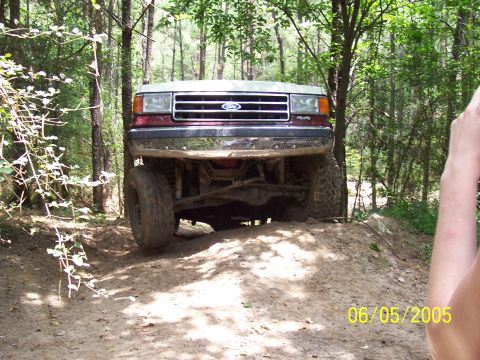 1990 Ford Bronco - A lifted Ford truck navigates an off-road trail on a sunny day.