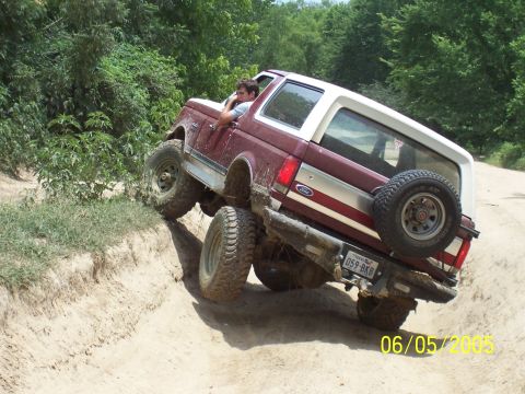 1990 Ford Bronco - 1990 Ford Bronco tackling a challenging off-road trail with a driver inside.