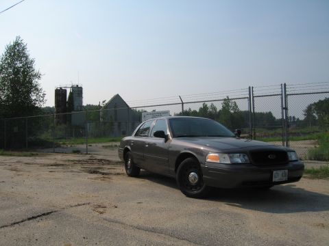 2001 Ford Crown Victoria - A 2001 Ford Crown Victoria police car is parked in front of an industrial site under a clear sky.