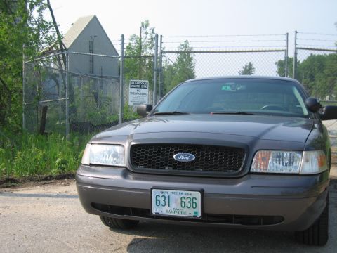 2001 Ford Crown Victoria - A 2001 Ford Crown Victoria is parked in front of a fenced-off area with a hazardous waste site sign.