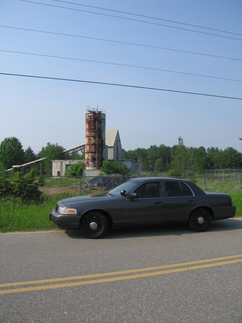 2001 Ford Crown Victoria - Grey Ford Crown Victoria Police Interceptor parked on the shoulder of a double-yellow-line road, shot in profile from the driver's side wit…