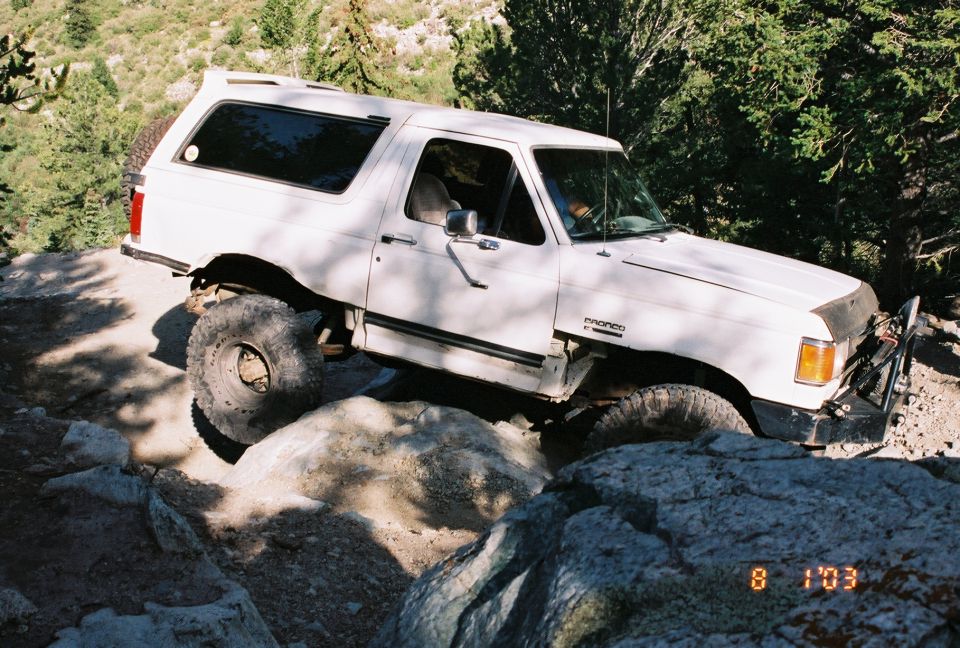 White Ford Bronco navigating rocky terrain, front-right tire visible