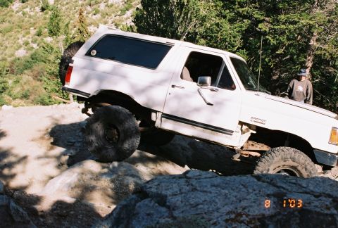 1996 Ford Bronco - A white 1996 Ford Bronco navigates a rocky trail, its off-road capabilities.