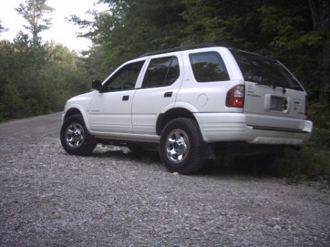 2000 Isuzu Rodeo - A white 2000 Isuzu Rodeo is parked on a gravel road surrounded by trees.