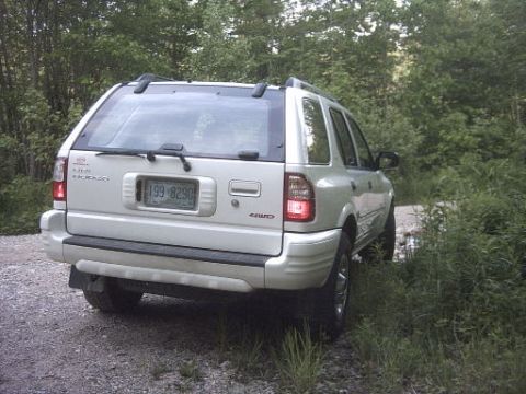 2000 Isuzu Rodeo - This 2000 Isuzu Rodeo is seen from the rear 3/4 angle on a gravel road surrounded by trees.