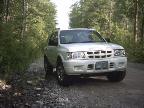 2000 Isuzu Rodeo - White 2000 Isuzu Rodeo on a gravel road surrounded by trees.