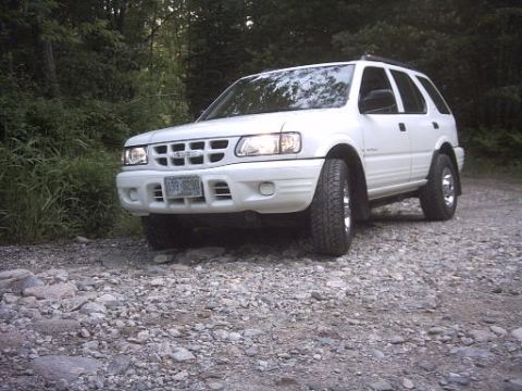 2000 Isuzu Rodeo - This white 2000 Isuzu Rodeo is parked on a rocky, unpaved road surrounded by trees.