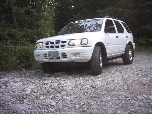 White four-door Isuzu SUV on a rocky gravel trail in the woods