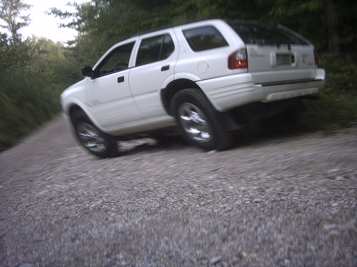 White 2000 Isuzu Rodeo SUV on a gravel road, right rear quarter view, tilted to the right