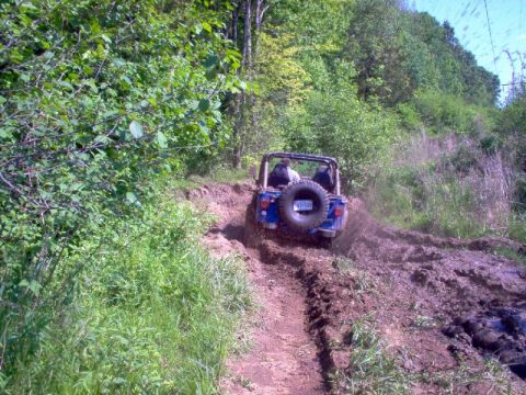 1976 GMC C/K Pickup - A blue Jeep Wrangler navigates a challenging muddy off-road trail, with the SuperMotors.net logo visible in the lower right corner.