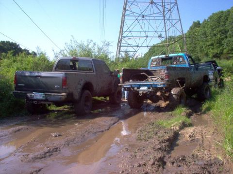 1976 GMC C/K Pickup - Two pickup trucks navigate a challenging muddy off-road course under a power line tower.