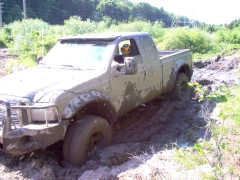 1976 GMC C/K Pickup - A pickup truck is stuck deep in mud, with the driver visible behind the wheel.