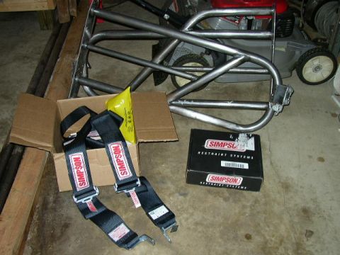 1995 Ford Bronco - A roll cage frame and Simpson restraint systems are laid out on a garage floor.