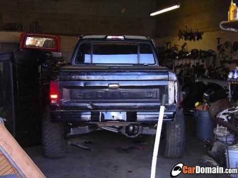 1990 Ford Bronco - Rear view of a dark Ford pickup with a 'FORD' stamped tailgate and lifted suspension parked in a cluttered garage.