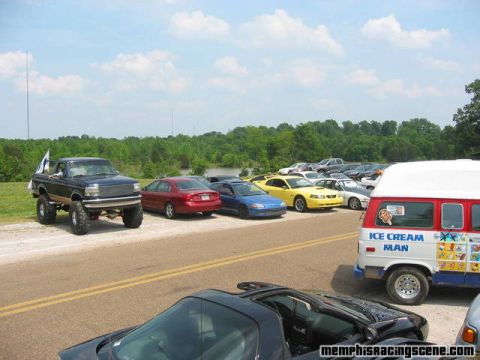 1978 Ford Bronco - A lifted pickup truck with large tires is parked on the grass next to a row of other vehicles.