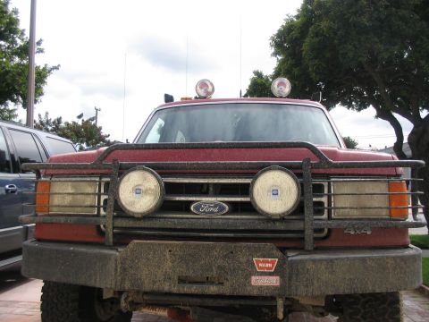 1989 Ford Bronco - Front view of a red Ford truck, equipped with a brush guard and off-road lights.