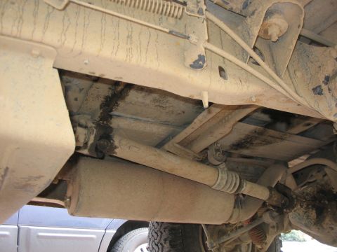 1989 Ford Bronco - The undercarriage of a vehicle is covered in dirt and grime, with visible mechanical components.