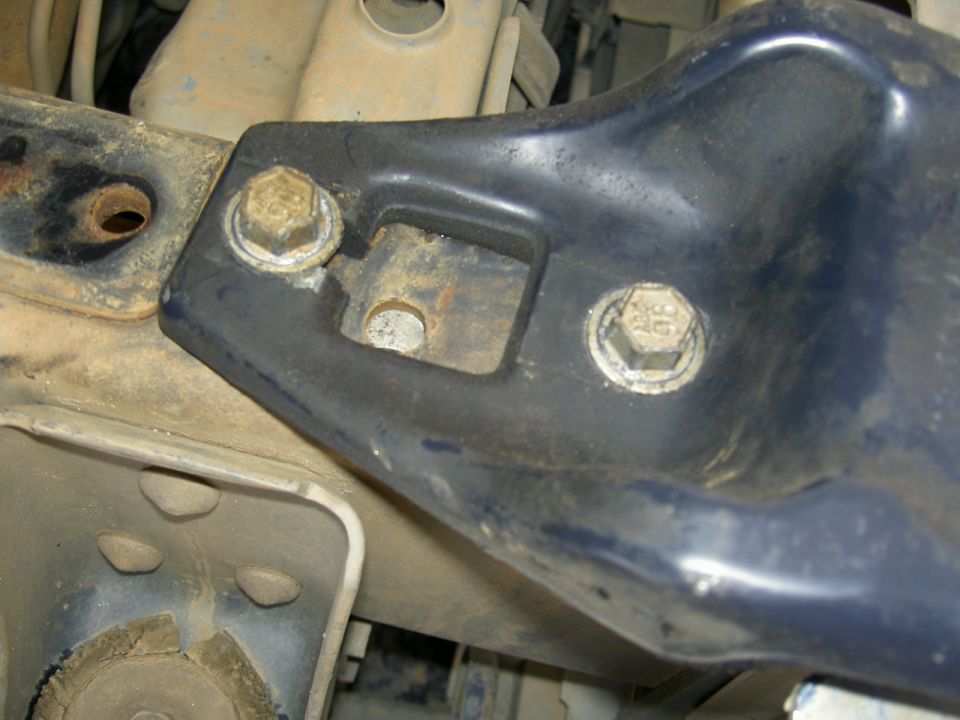 Close-up of black steel frame bracket bolted to a dusty chassis with two hex bolts
