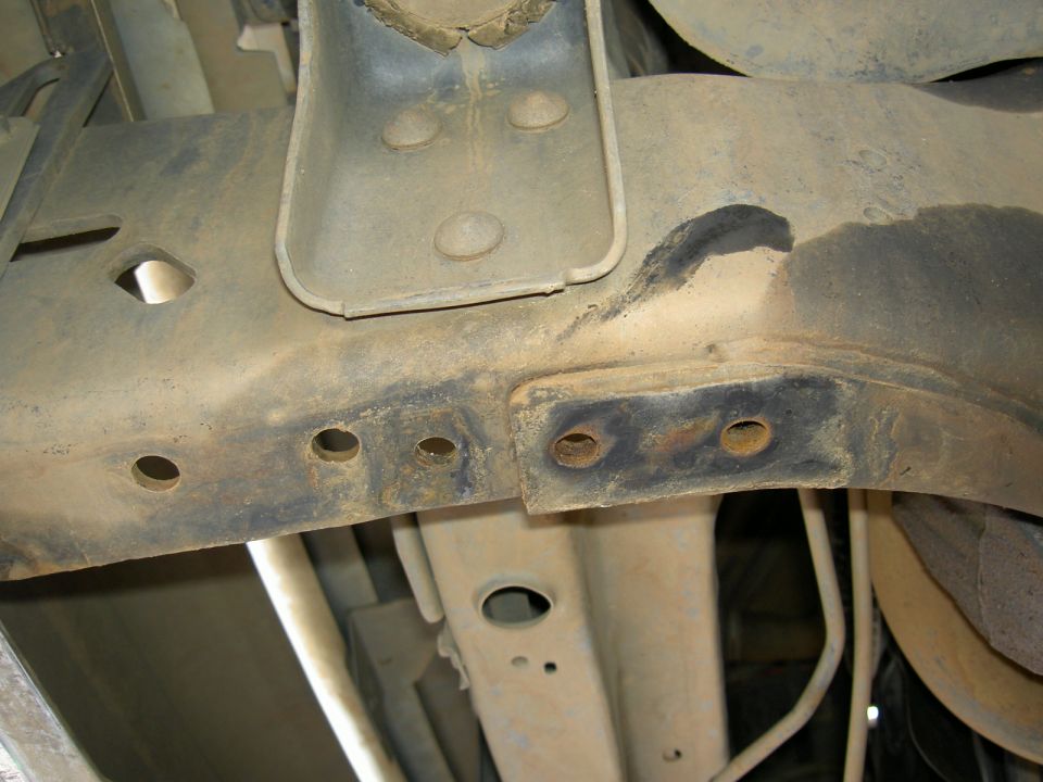 Underside close-up of a truck frame rail with a welded fabricated bracket and open bolt holes