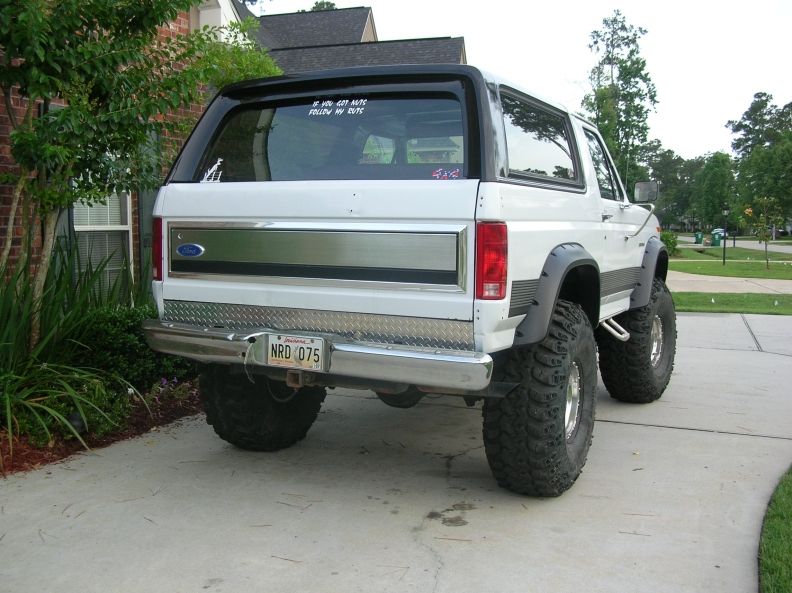 Rear of a white lifted Ford Bronco on big mud tires parked in a driveway