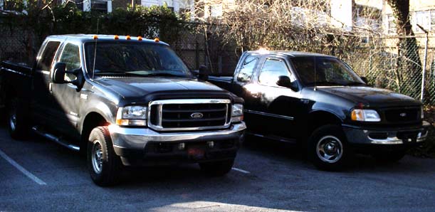 Black Ford F-250 Super Duty crew cab parked beside a black F-150 in a fenced lot