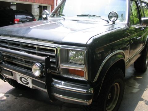 1986 Ford F-150 - Dark Ford F-Series truck with auxiliary lights and a brush guard is parked outside.