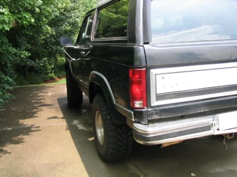 1986 Ford F-150 - This black Ford Bronco is shown from the rear quarter angle, a lifted suspension and off-road tires.