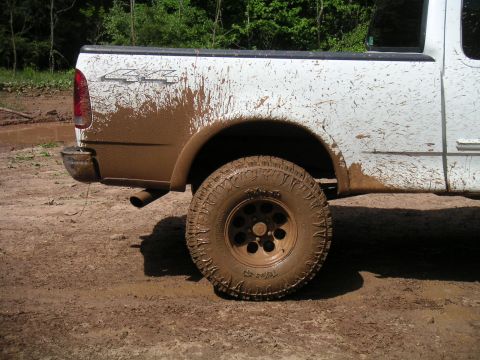 1994 Ford Bronco - White pickup truck covered in mud after driving off-road. The rear wheel and fender are heavily soiled.