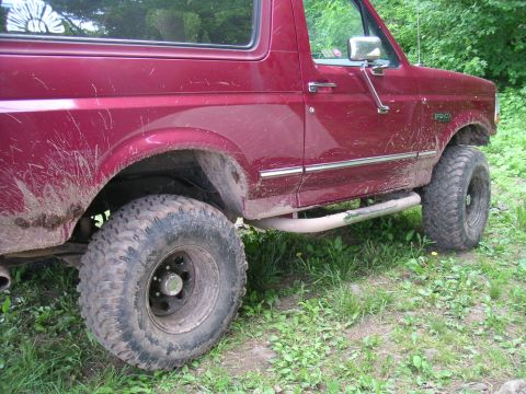 1994 Ford Bronco - A maroon Ford Bronco is shown from the front quarter, covered in mud from off-road use.