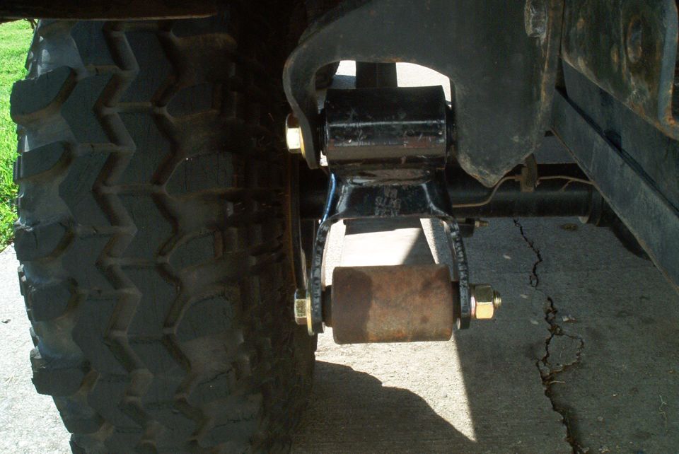 Close-up of a rear leaf-spring shackle and lift block above an off-road tire on a truck