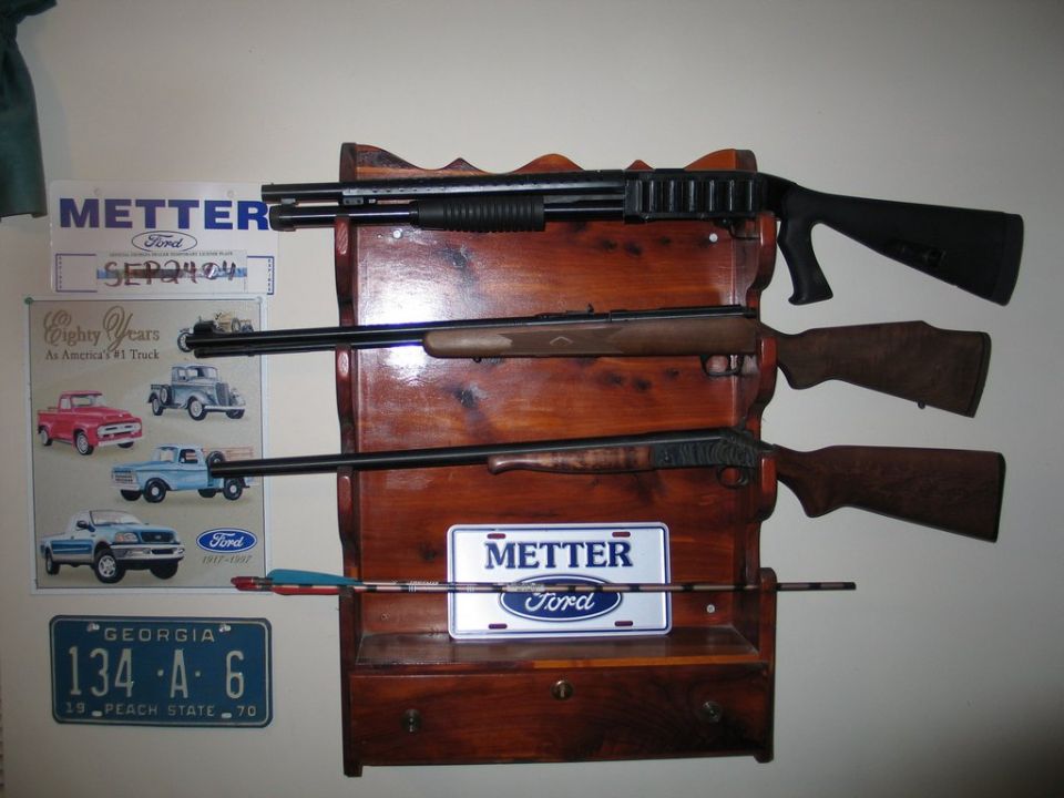 Wooden gun rack on a wall beside Ford dealer plates, a 1970 Georgia plate and a Ford truck sign