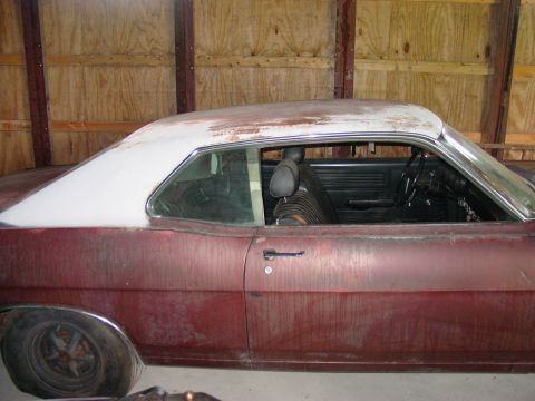 1969 Ford Fairlane - A 1969 Ford Fairlane coupe in maroon with a white roof, seen from the side inside a wooden structure.