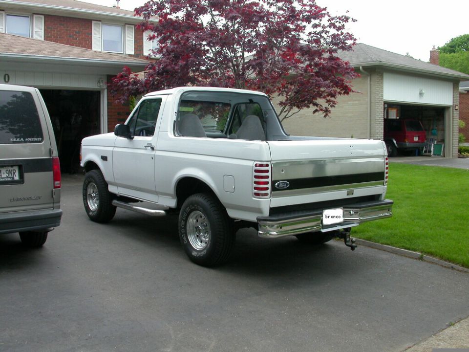 White Ford Bronco with rear top removed, viewed from rear driver's side in a driveway
