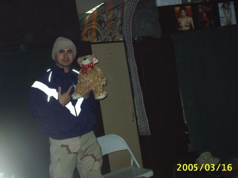 1988 Mercury Sable - A man poses with a teddy bear in a dimly lit room with posters on the wall.