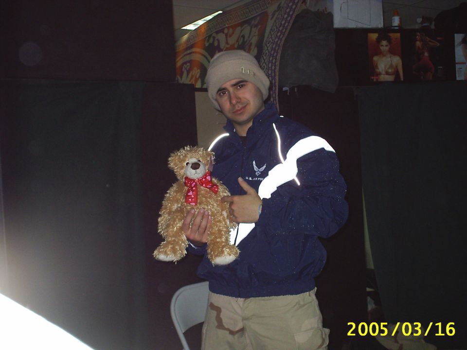 Person in an Air Force jacket and beanie holding a tan teddy bear indoors