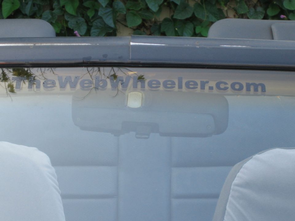 Car interior with "TheWebWheeler.com" text on windshield and grey seat covers