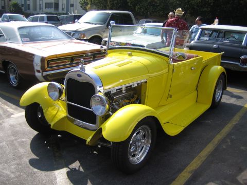 1985 Ford Mustang - A bright yellow Model A-style roadster pickup hot rod sits at an outdoor car show, shot from the front three-quarter angle with its side ho…