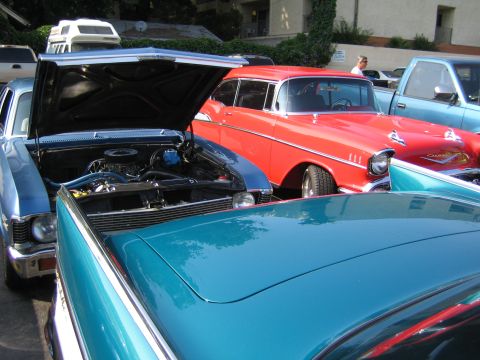 1985 Ford Mustang - A red 1957 Chevrolet Bel Air is parked next to a blue classic car, with another car visible in the background.