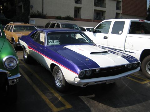 1985 Ford Mustang - A classic Dodge Challenger is parked in a lot with other vehicles, displaying a 'For Sale' sign.