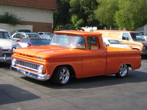 1985 Ford Mustang - A bright orange pickup truck is parked in a lot, surrounded by other vehicles.