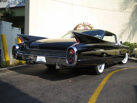 1985 Ford Mustang - The distinctive tail fins and chrome details of a classic 1959 Cadillac Eldorado are visible from the rear quarter.