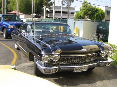 1985 Ford Mustang - A black 1959 Cadillac Coupe de Ville is parked next to a blue Ford Ranger pickup truck.