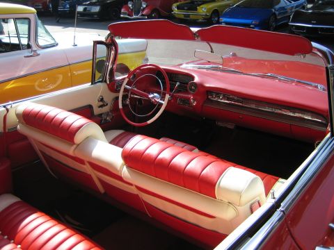 1985 Ford Mustang - The interior of a red convertible with white accents is visible, with other cars in the background.