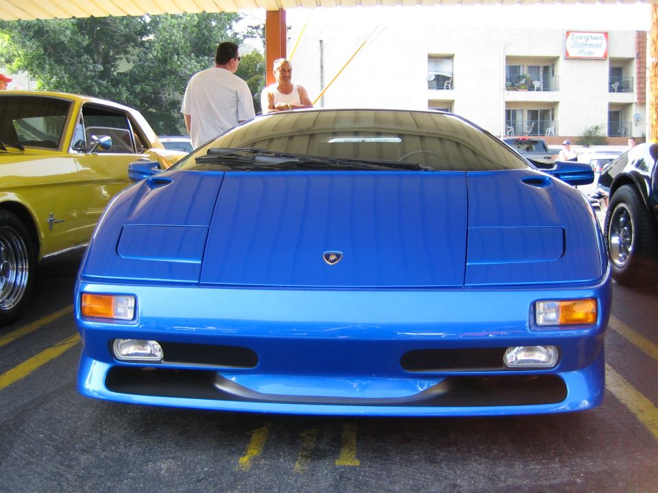 Blue Lamborghini Diablo front view, parked under a canopy next to a yellow Ford Mustang