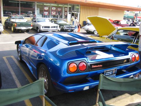 1985 Ford Mustang - A blue Lamborghini Diablo is parked in front of a store, with other vehicles in the background.