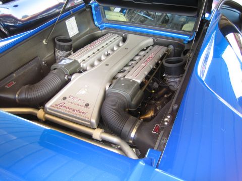 1985 Ford Mustang - The engine bay of a blue Lamborghini is shown, highlighting the V12 5.7L engine and its timing management system.