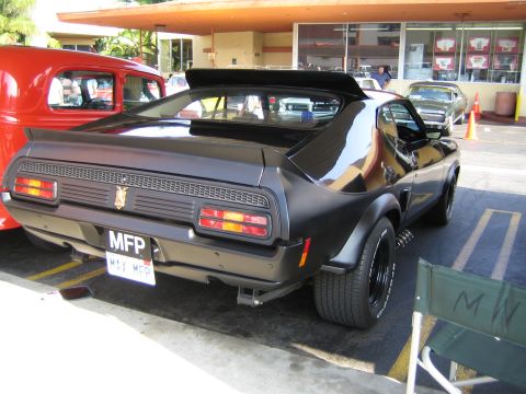 1985 Ford Mustang - A black coupe with a prominent rear spoiler and custom license plates is parked next to a red vehicle.